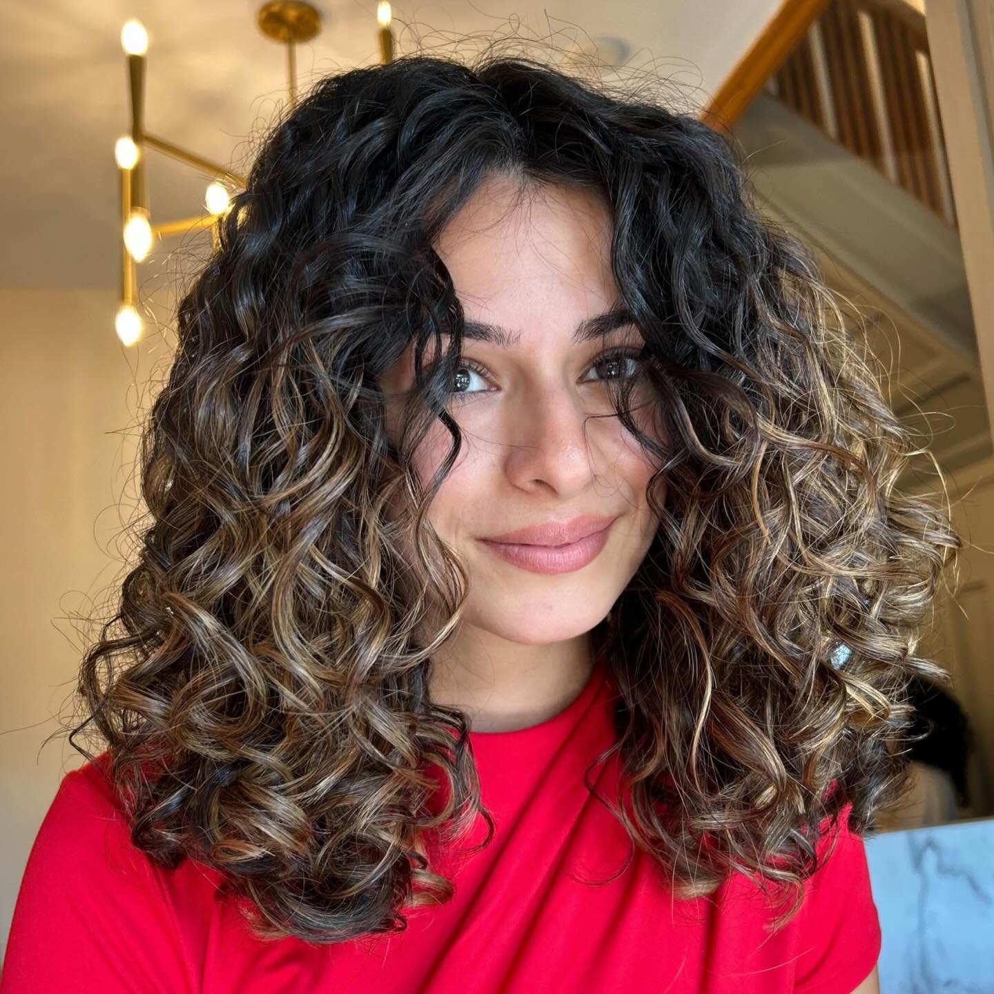 Voluminous Dark Brown Curly Haircut with Golden Highlights and Layered Ringlets