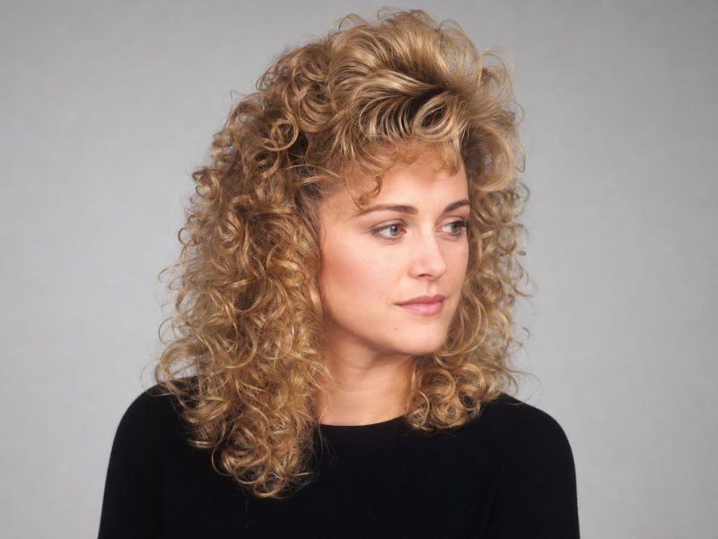 Voluminous 80s Perm with Teased Crown and Side-Swept Bangs on Dark Blonde Hair
